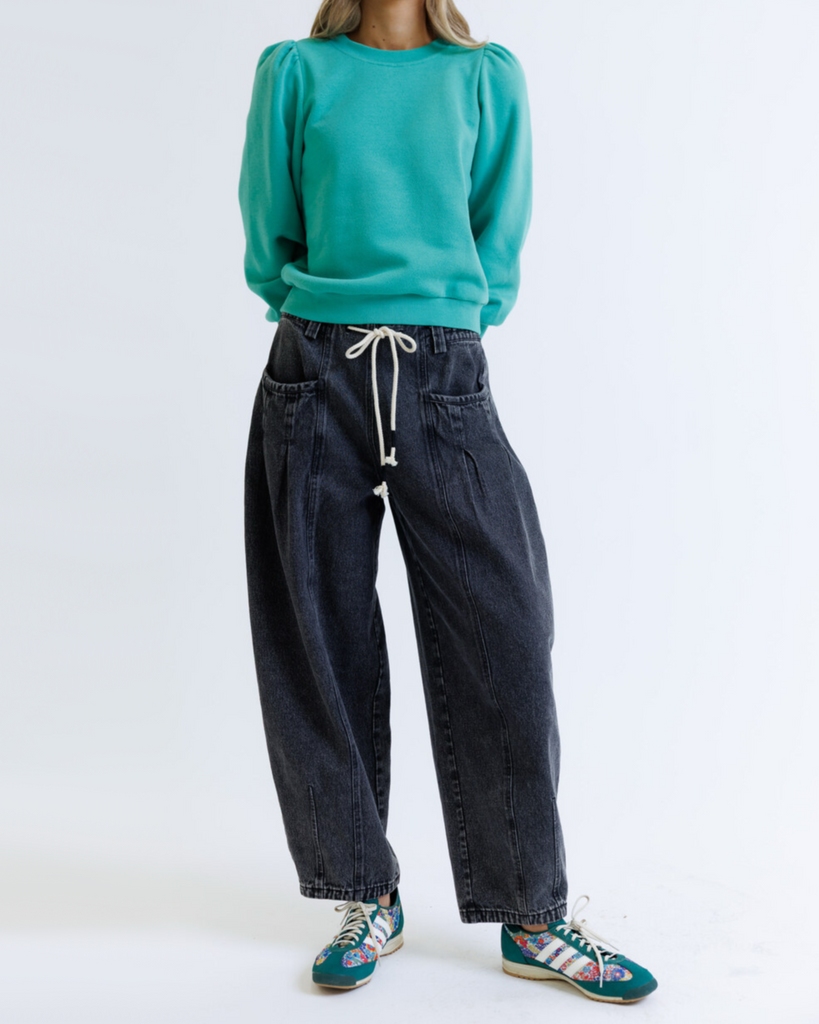 Woman wearing a teal sweatshirt and black jeans on a white background