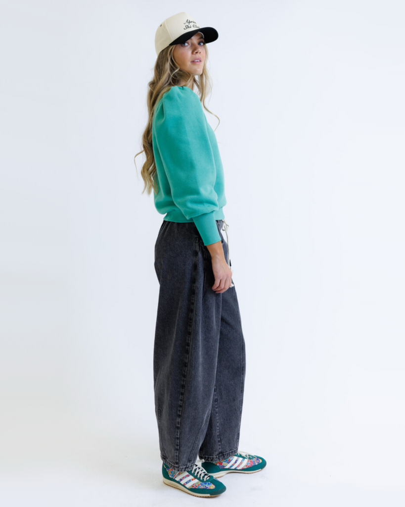 Woman wearing a teal sweatshirt and black jeans on a white background