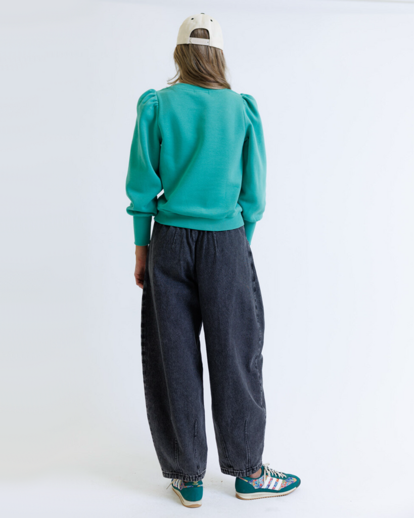 Woman wearing a teal sweatshirt and black jeans on a white background
