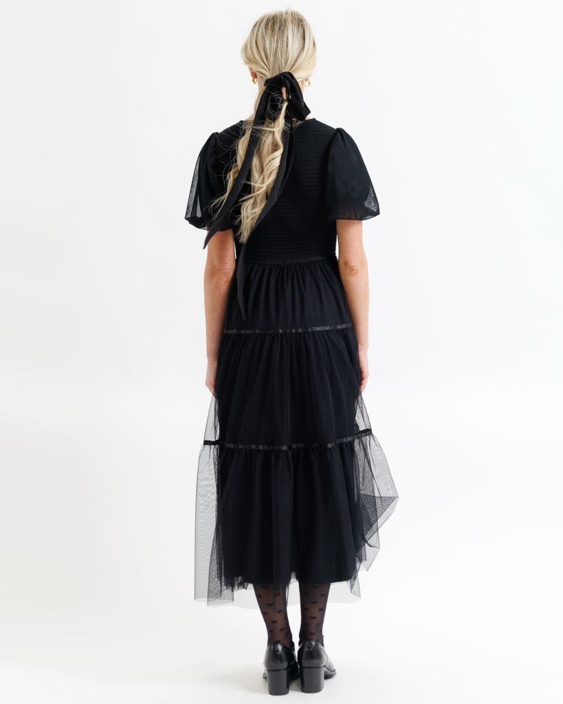 Woman wearing a black dress with tulle overlay on a white background