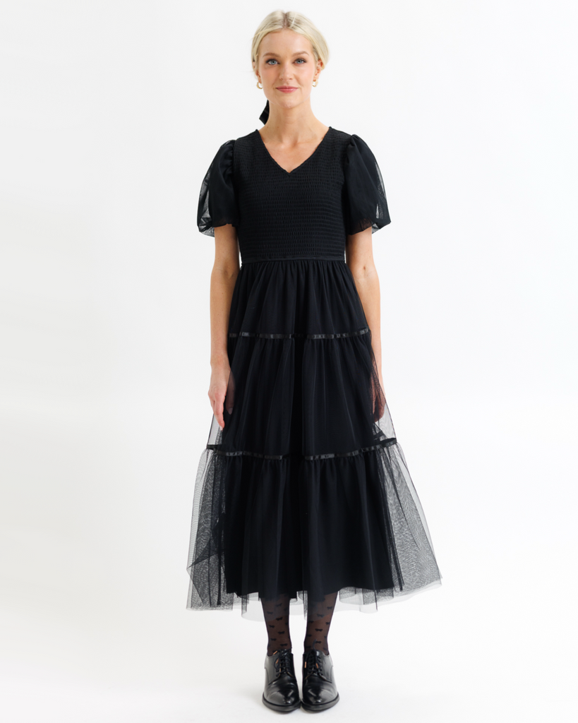 Woman wearing a black dress with tulle overlay sleeves and skirt on a white background