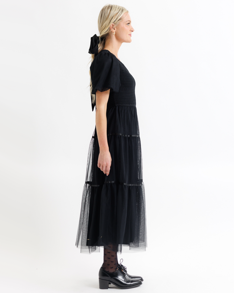 Woman wearing a black dress with tulle overlay on a white background