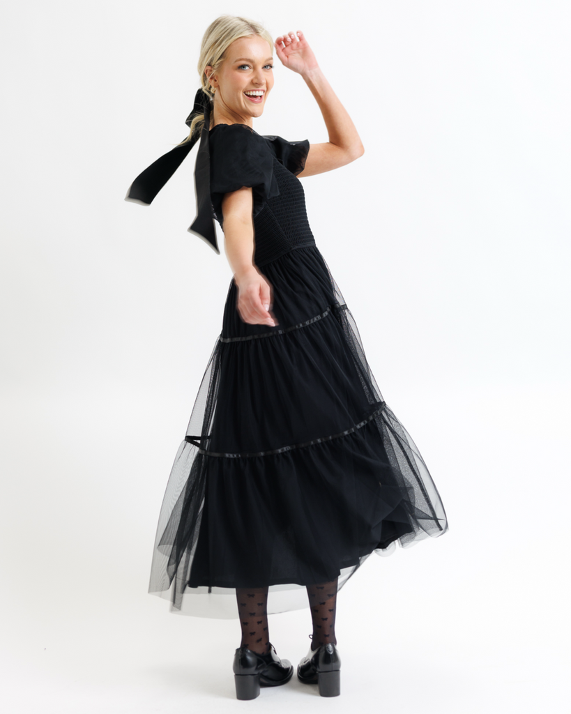 Woman wearing a black dress with tulle overlay sleeves and skirt on a white background