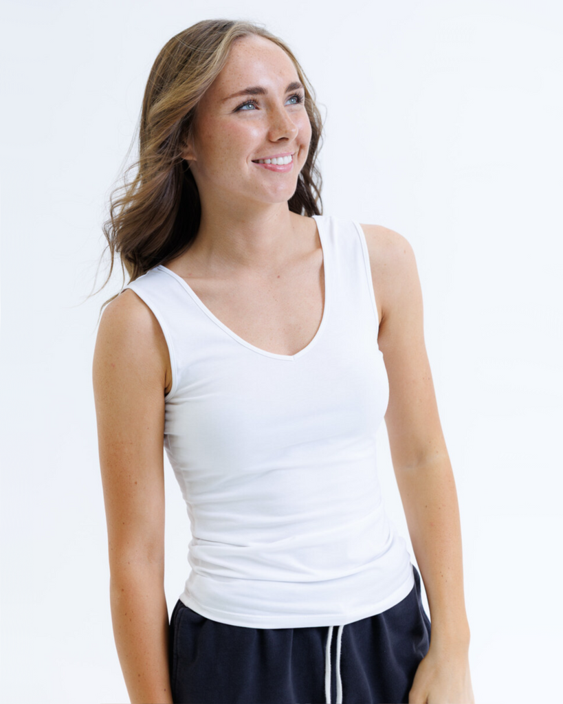 Woman wearing a white layering tank top and dark pants on a white background