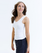 Woman wearing a white layering tank top and dark pants on a white background