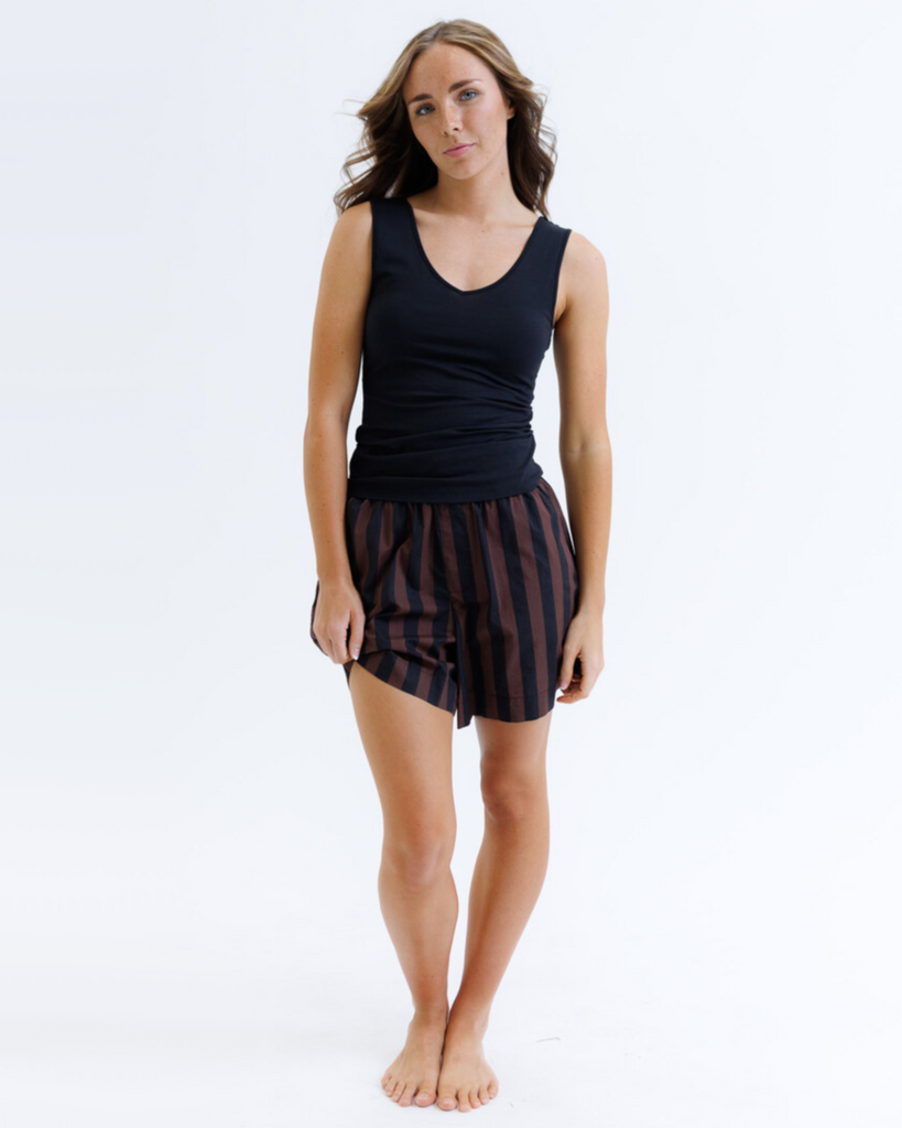 Woman wearing a black layering tank top and striped shorts against a white background