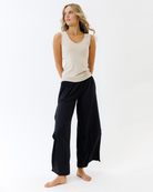 Woman wearing a beige tank top and black wide-leg pants on a white background