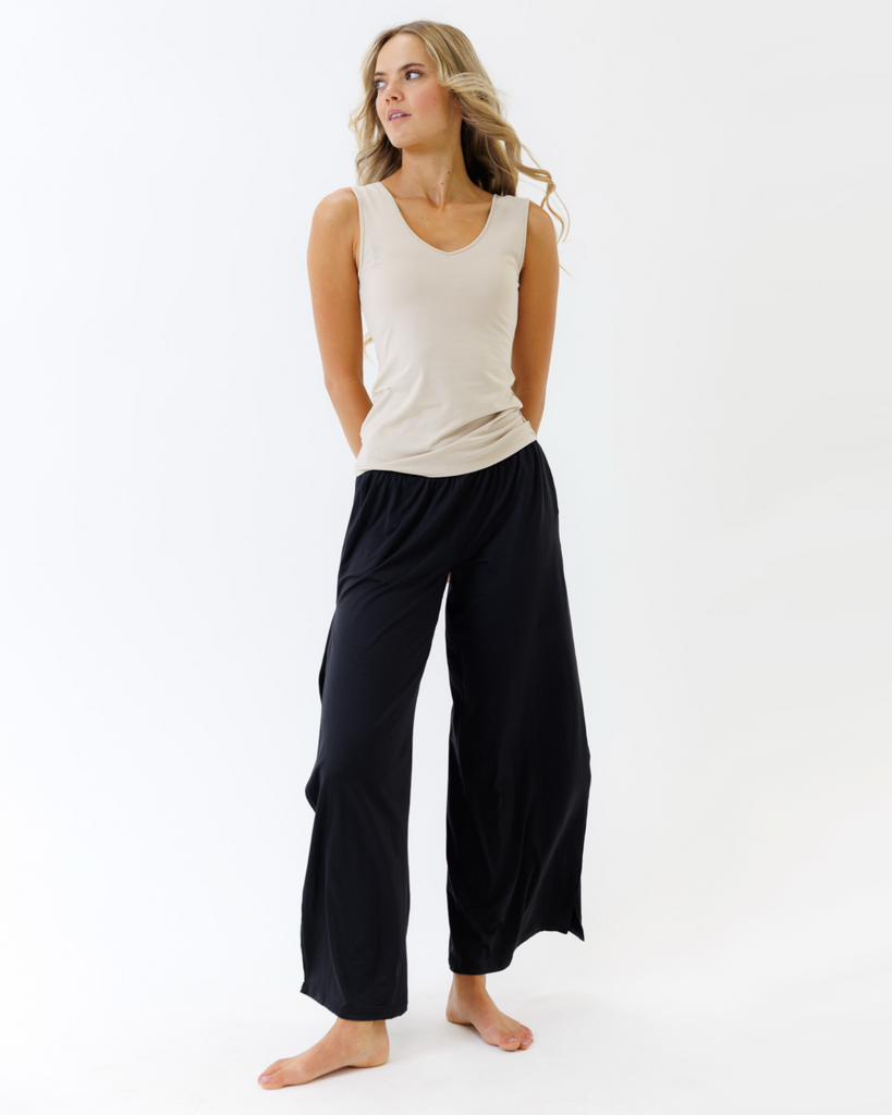 Woman wearing a beige tank top and black wide-leg pants on a white background