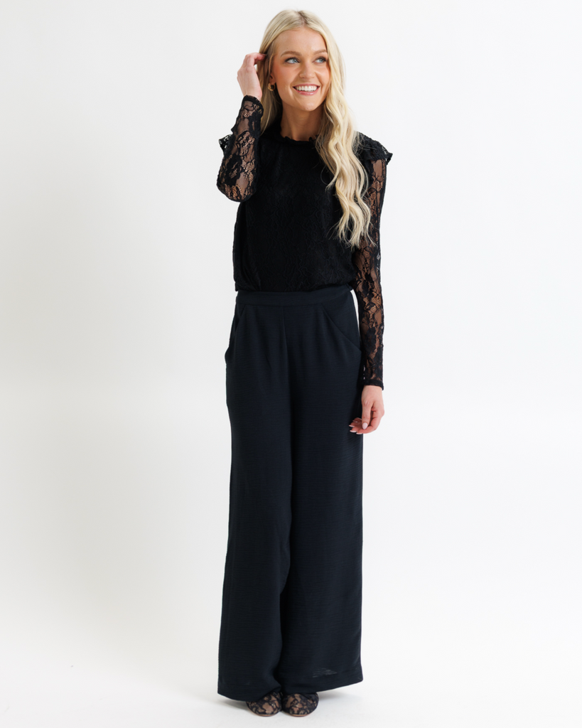 Woman wearing a black shirt with lace sleeves and black pants on a white background