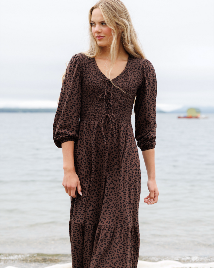 Woman wearing a brown dress with black cheetah print standing by the ocean.