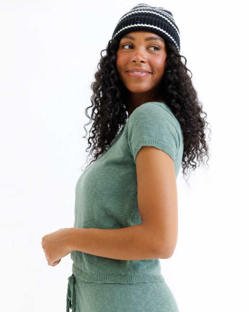 Woman wearing a green sweater top and black and white striped beanie on a white background
