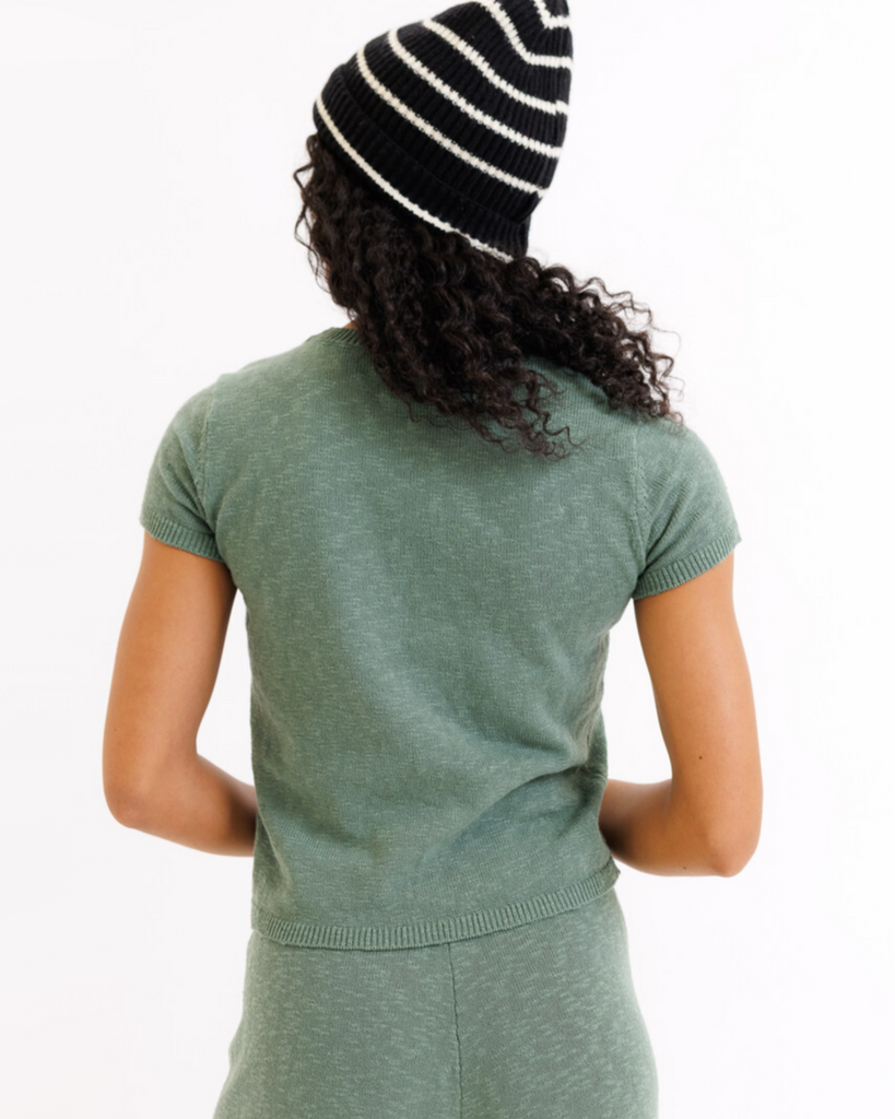 Woman wearing a green sweater top and black and white striped beanie on a white background