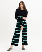 Woman wearing a black sweater and striped pants with green accents on a white background