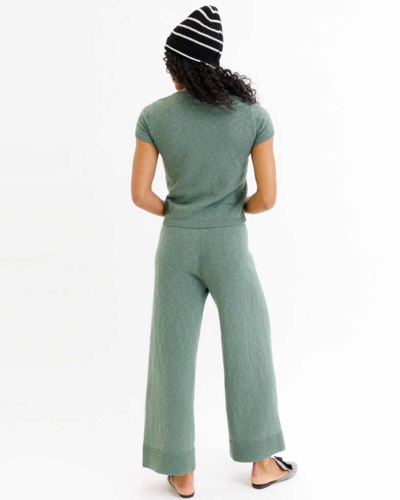 Woman wearing a green matching top and wide-leg bottom set with a striped beanie on a white background