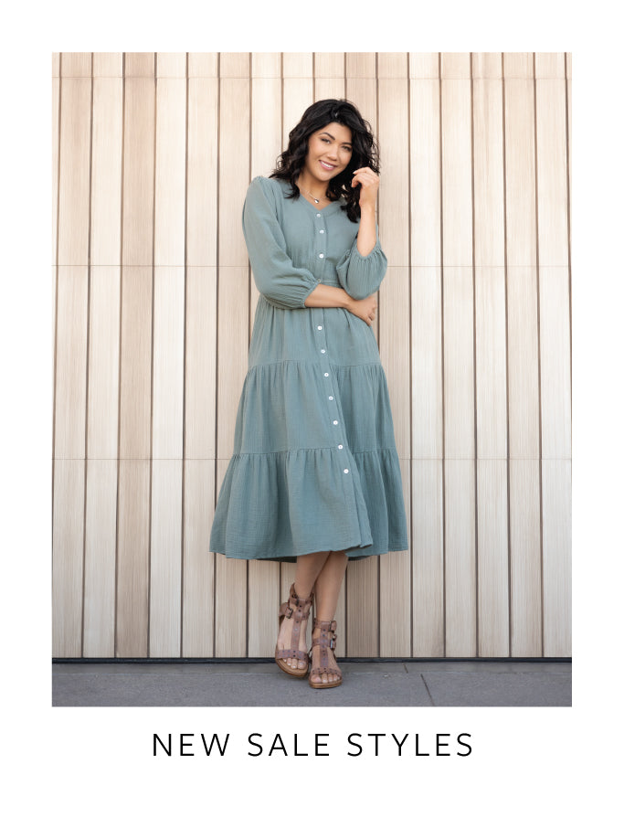 Woman wearing a teal dress standing against a wooden paneled wall with 'New Sale Styles' text.