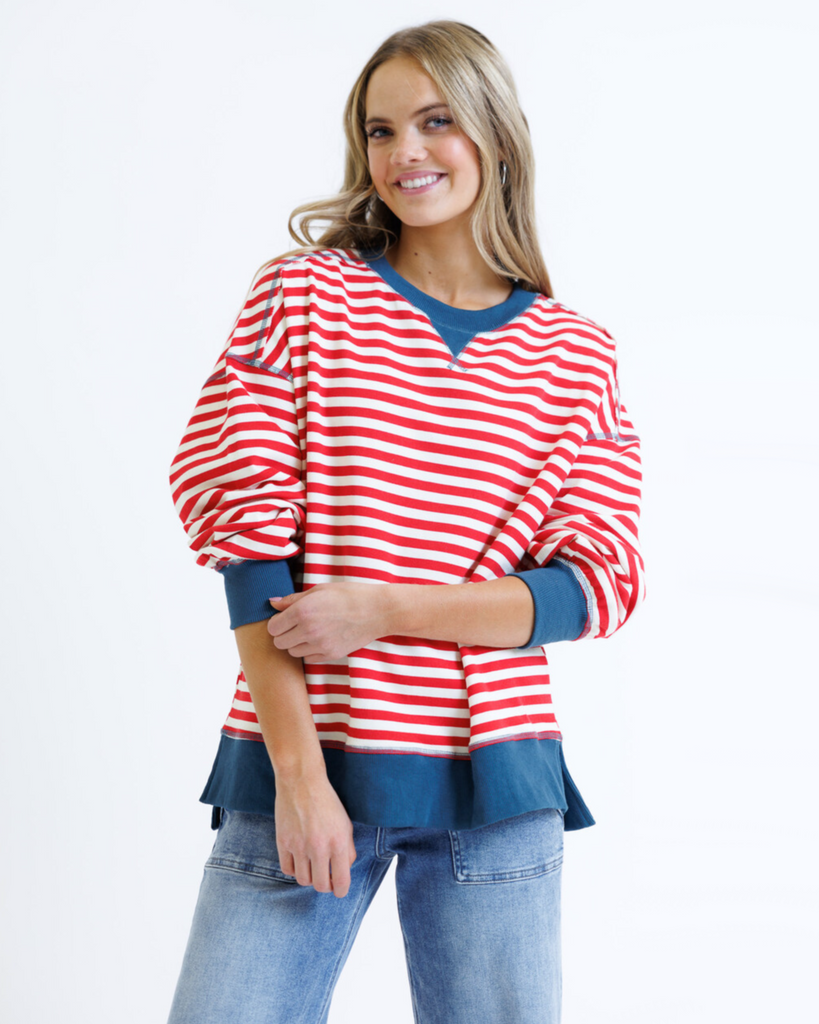 Woman wearing a red striped sweatshirt with blue accents and light denim jeans on a white background