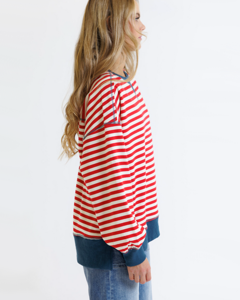 Woman wearing a red striped sweatshirt with blue accents and light denim jeans on a white background