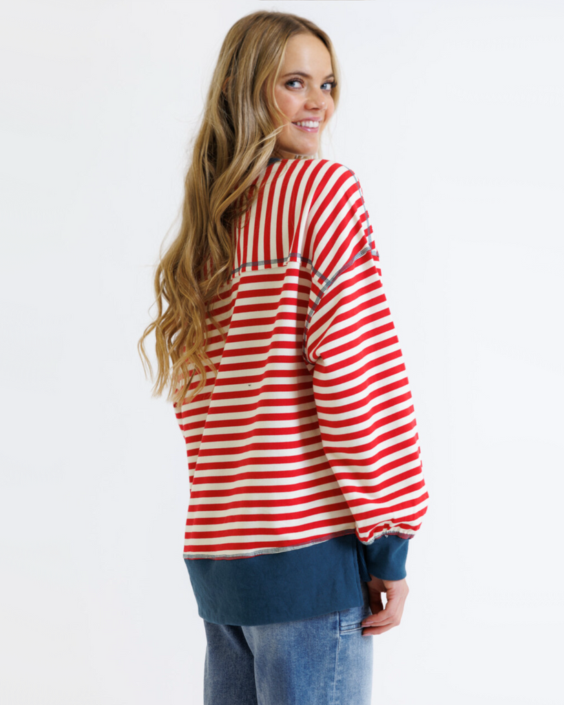 Woman wearing a red striped sweatshirt with blue accents and light denim jeans on a white background