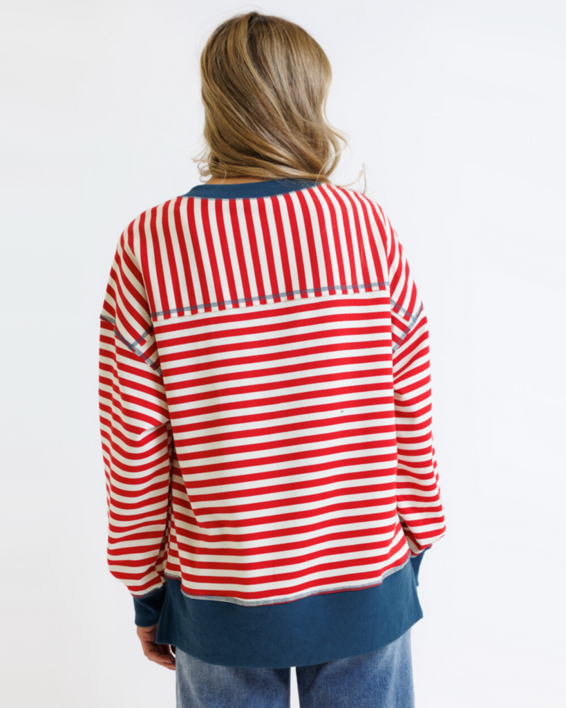 Woman wearing a red striped sweatshirt with blue accents and light denim jeans on a white background