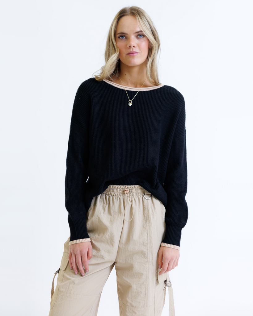 Woman wearing a black sweater and beige pants on a white background