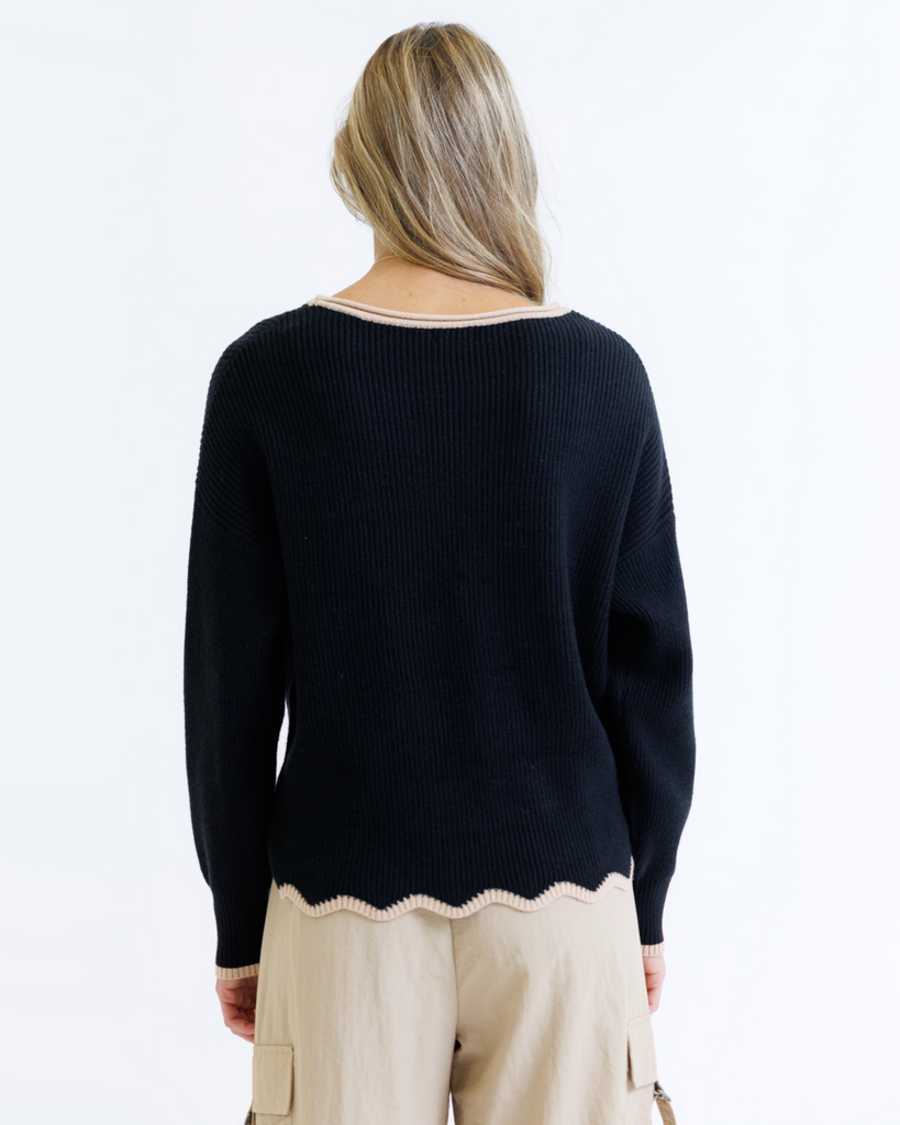 Person wearing a black sweater with a scalloped hem on a white background