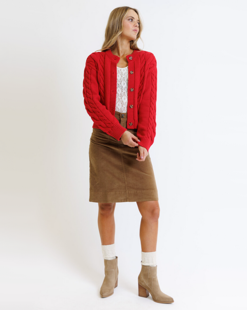 Woman wearing a red cardigan, brown skirt, and beige boots on a white background