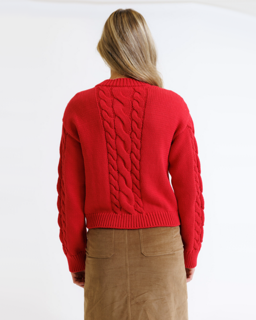 Woman wearing a red cable knit sweater on a white background