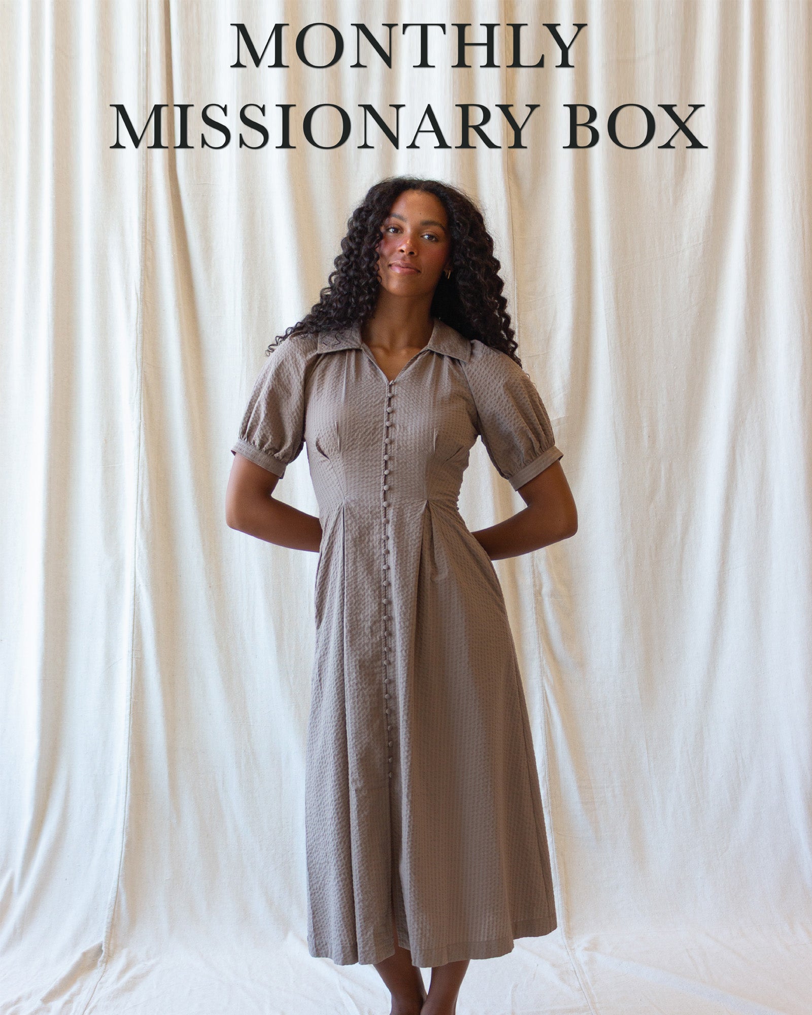 A woman stands against a draped cream fabric backdrop wearing a short-sleeve button-front midi dress in a light taupe-beige color. Large text at the top reads 'MONTHLY MISSIONARY BOX'.