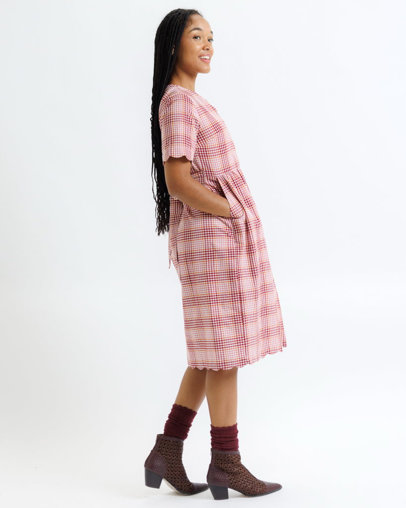 Woman wearing a pink plaid dress with brown boots on a white background