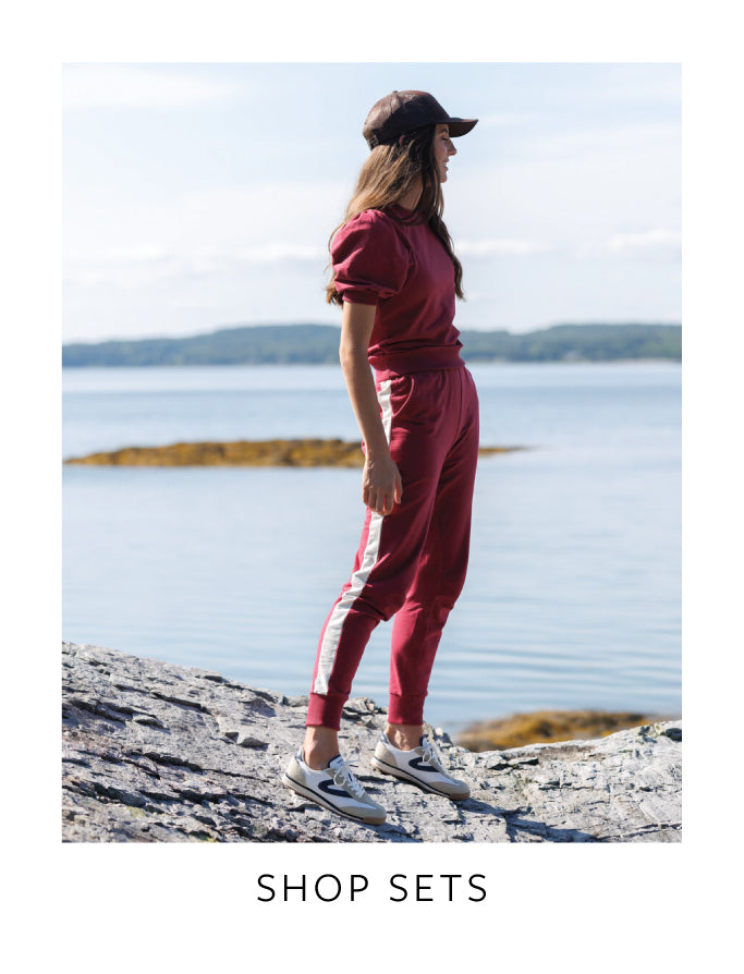 Woman in red outfit standing by a lake with text 'Shop Sets'.