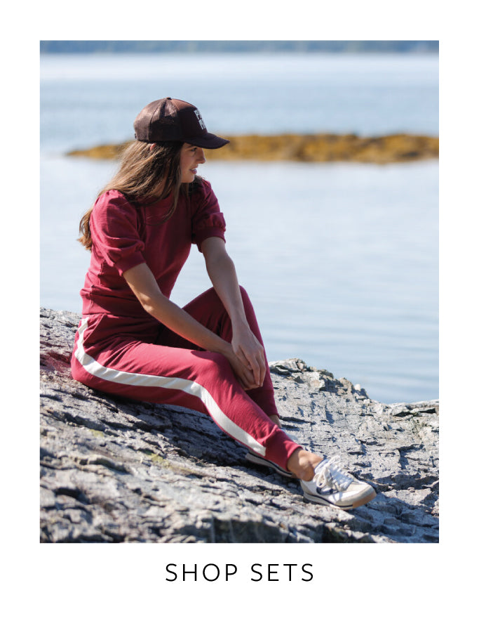 Woman sitting on a rock by a body of water wearing a red outfit with white stripes.