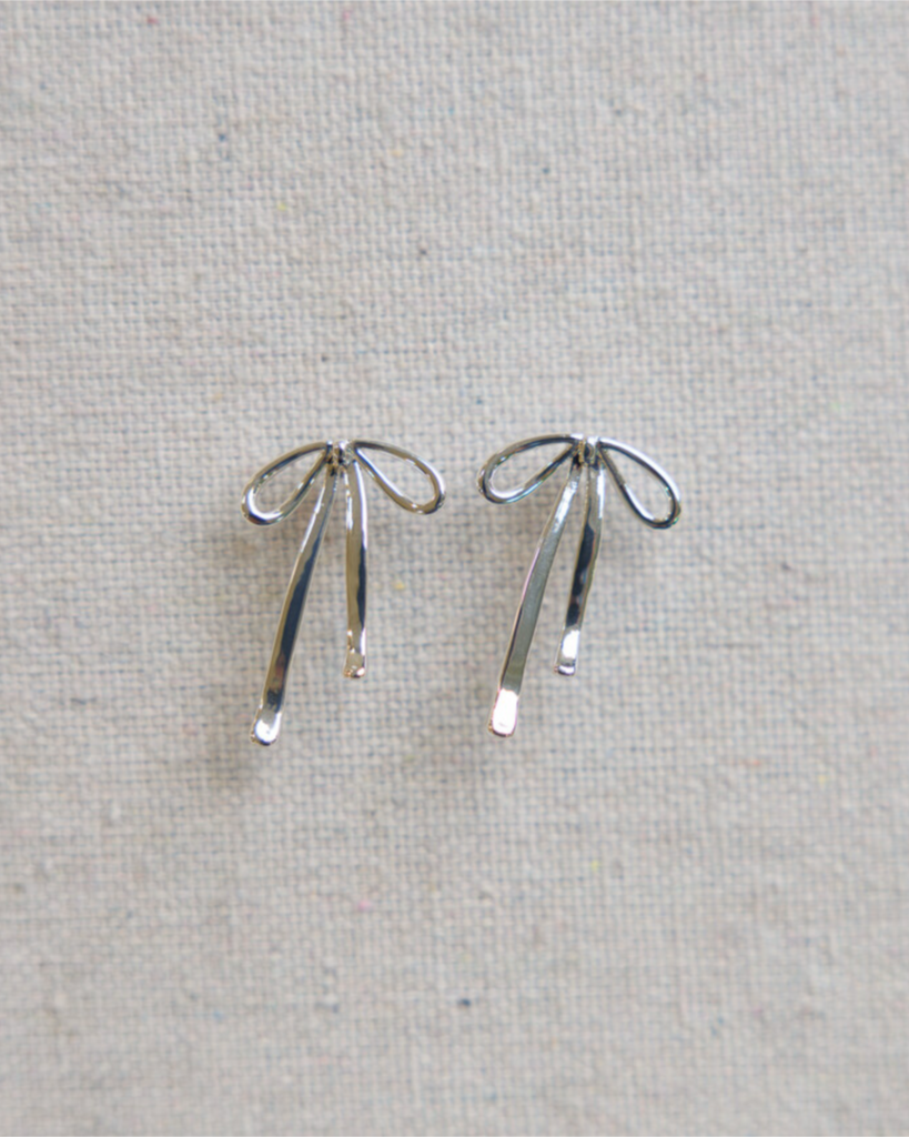Pair of silver bow-shaped earrings on a textured gray background