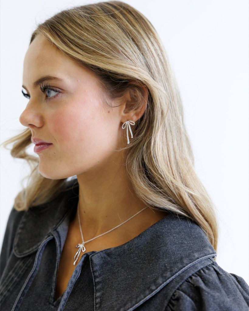Woman wearing a silver bow-shaped necklace and earrings on a white background