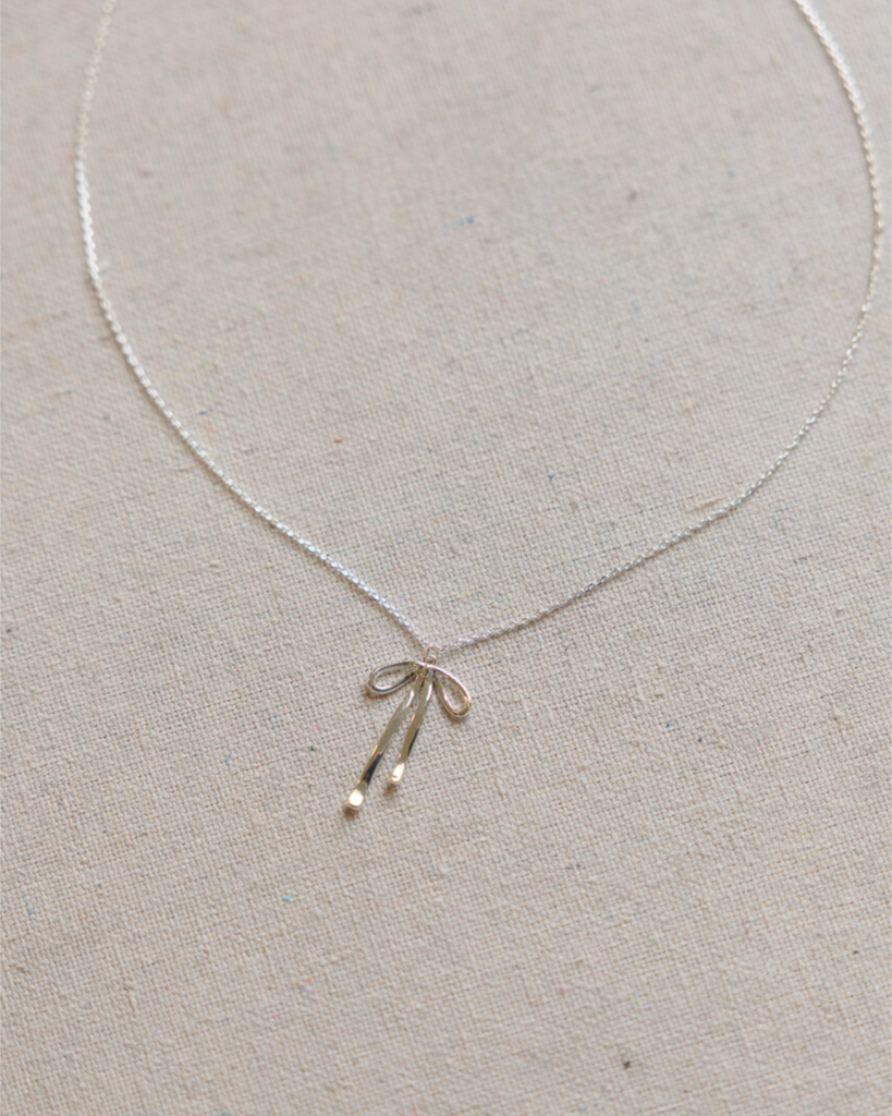 Silver necklace with a bow pendant on a light gray background