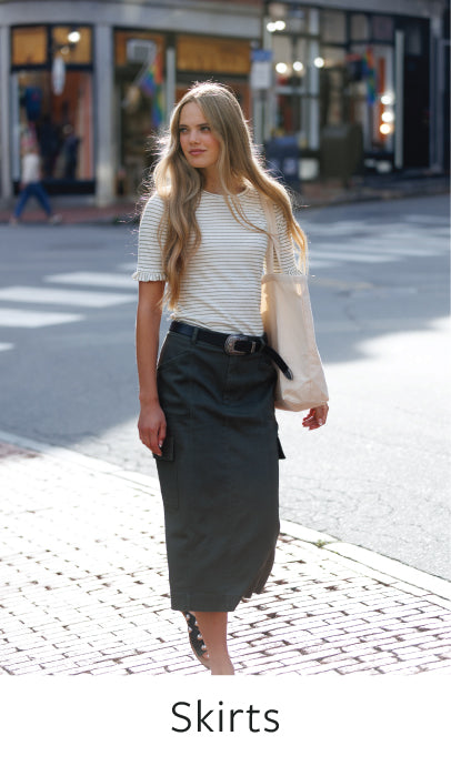 Woman walking on a street wearing a long skirt with text 'Skirts' at the bottom.