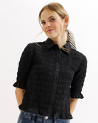 Woman wearing a black textured blouse with ruffled details on a white background