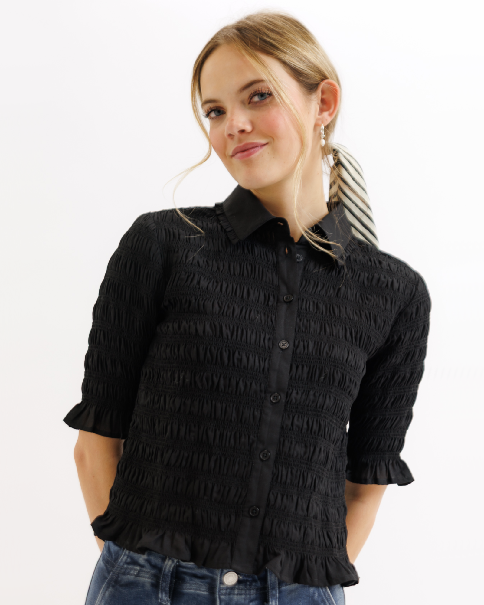 Woman wearing a black textured blouse with ruffled details on a white background