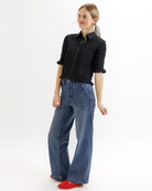 Woman wearing a black textured blouse with ruffled details and blue jeans on a white background