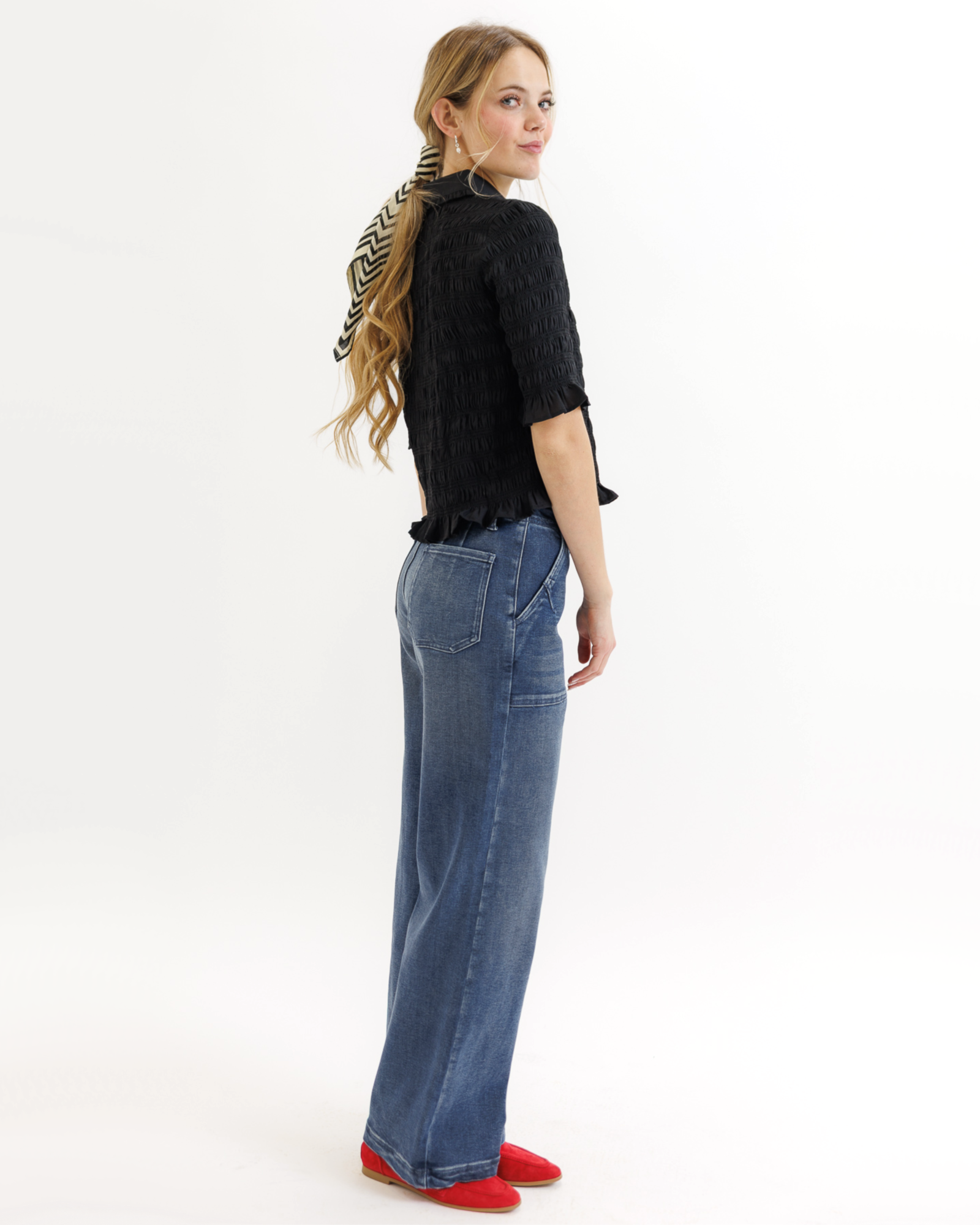 Woman wearing a black textured blouse with ruffled details and blue jeans on a white background