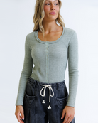 Woman wearing a green long-sleeve top and dark jeans on a white background