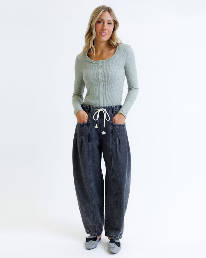 Woman wearing a green long-sleeve top and dark jeans on a white background