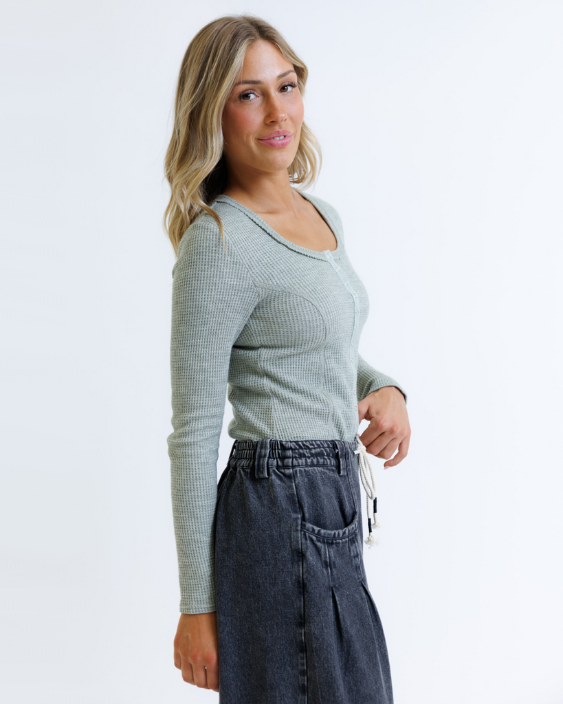 Woman wearing a green long-sleeve top and dark jeans on a white background