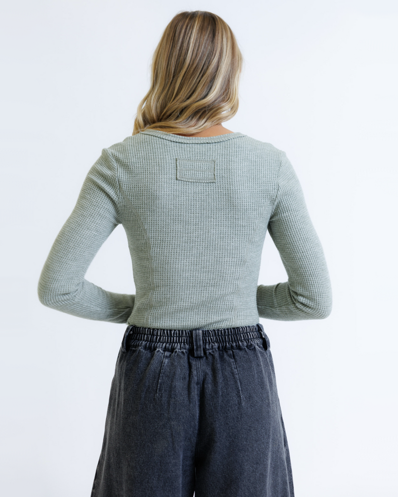 Woman wearing a green long-sleeve top and dark jeans on a white background