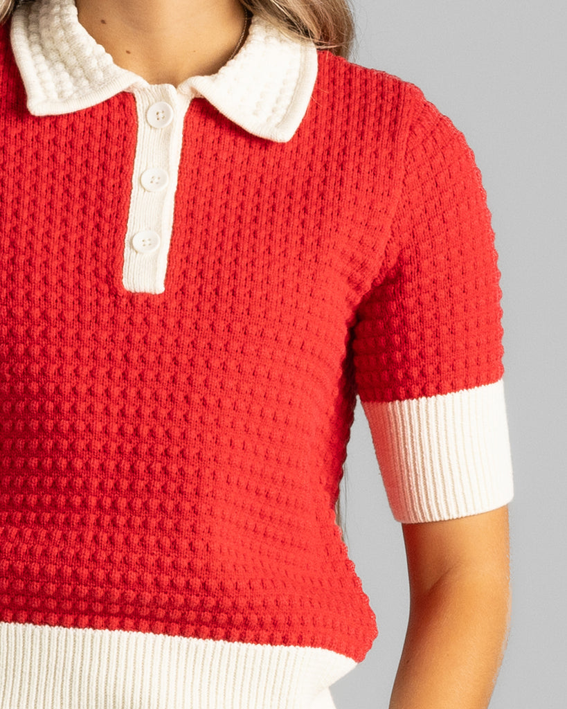 Model wearing a red with white details, short sleeve, collared, textured sweater.