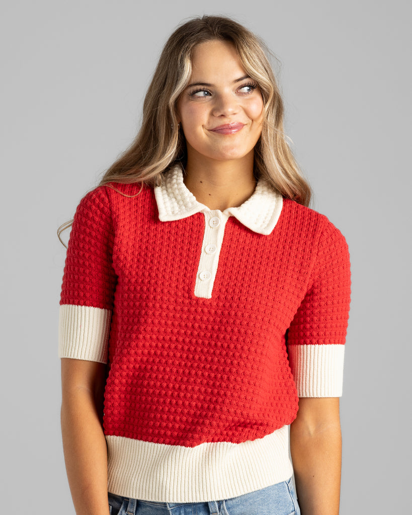 Model wearing a red with white details, short sleeve, collared, textured sweater.