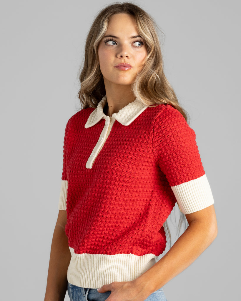 Model wearing a red with white details, short sleeve, collared, textured sweater.