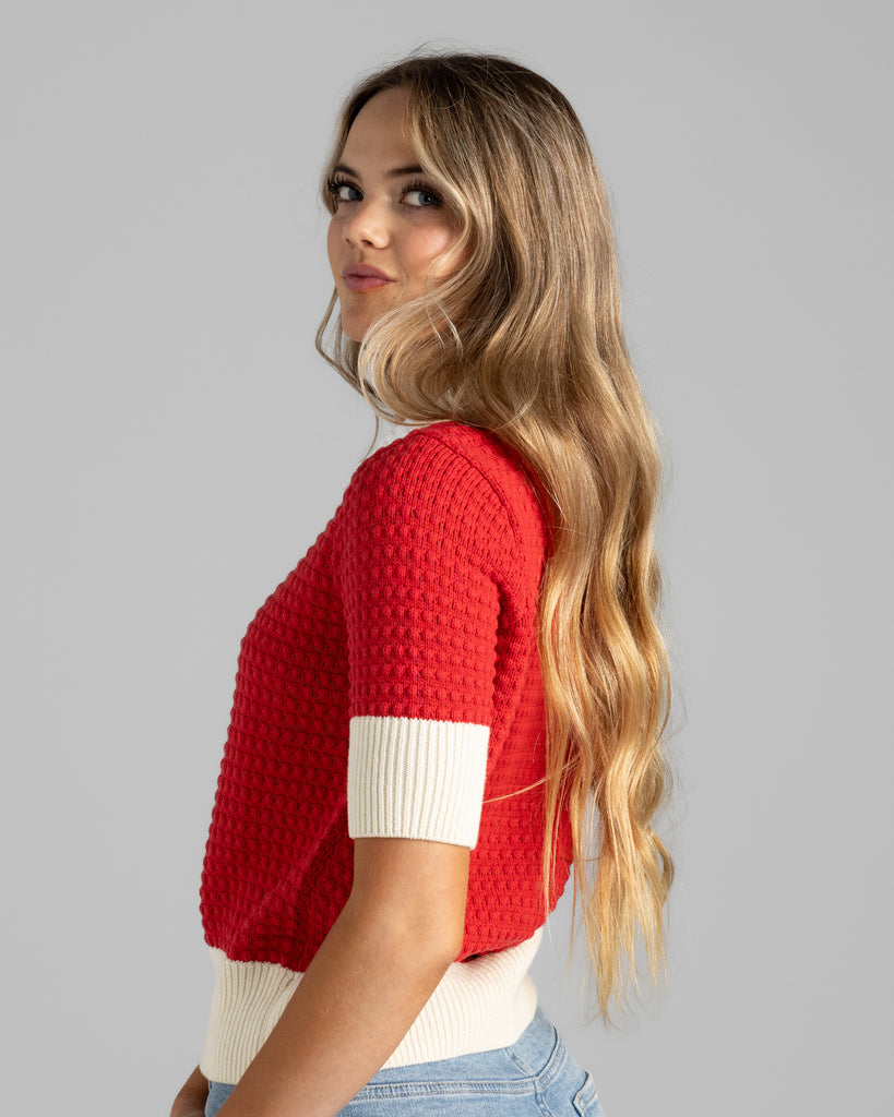 Model wearing a red with white details, short sleeve, collared, textured sweater.