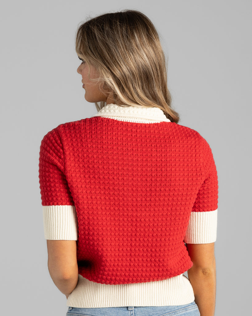 Model wearing a red with white details, short sleeve, collared, textured sweater.