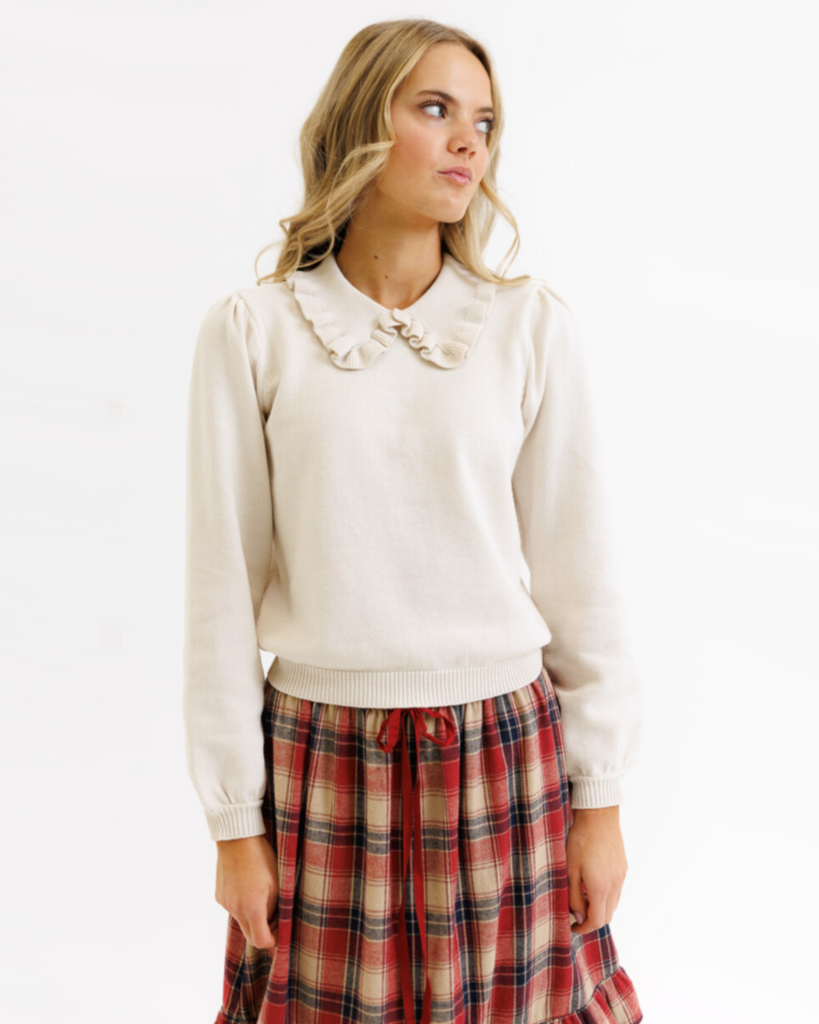 Woman wearing a cream colored sweater with a plaid skirt on a white background