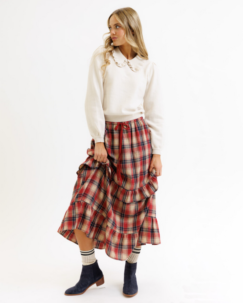 Woman wearing a cream colored sweater with a plaid skirt on a white background